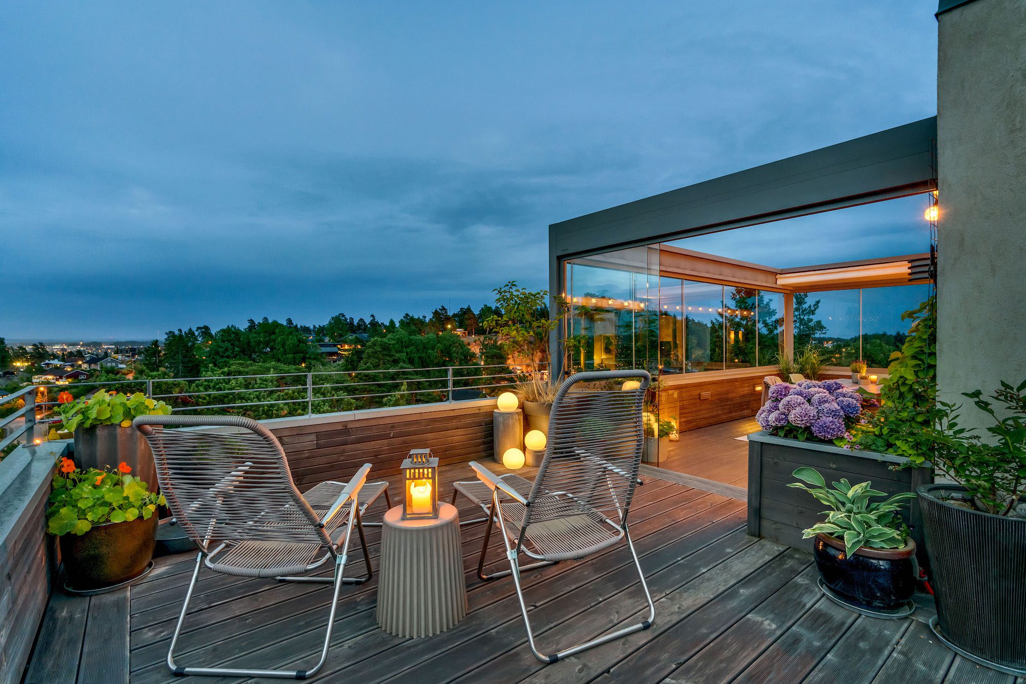 varen kommer tidligere med en pergola fra utedesign Komfortable utemøbler ved siden av en vakker pergola med en glass skyvedør og glassvegger, med utsikt over en by, bygget av uteDESIGN