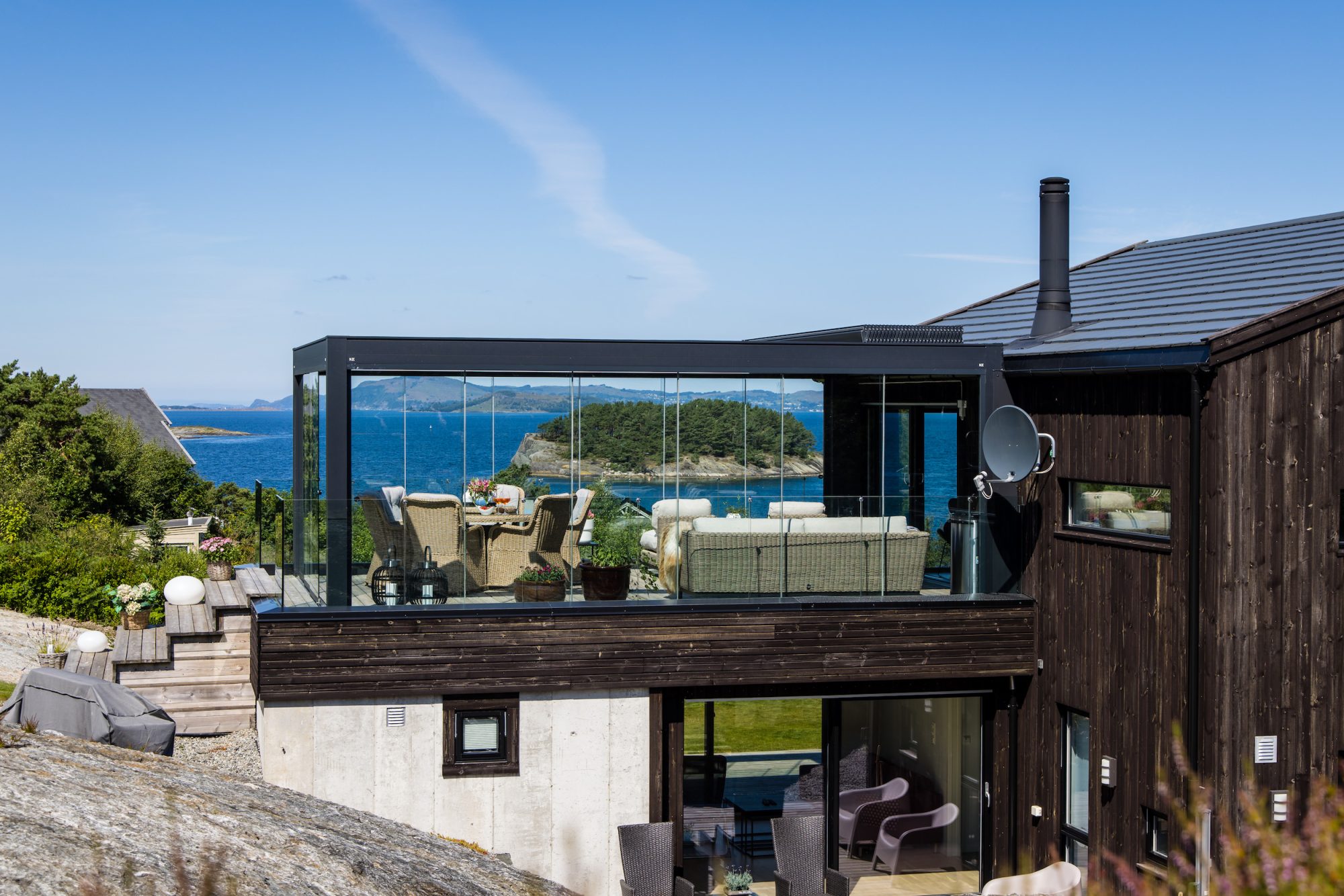 Et vakkert glasspergola med et lamelltak bygget av uteDESIGN ved siden av et norsk hus