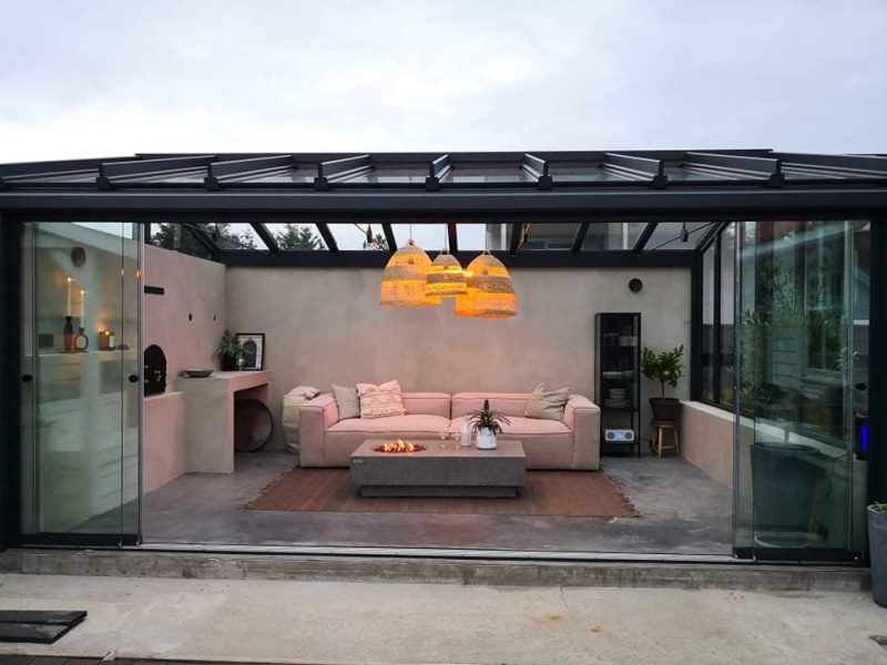 Bildet av en utestue innredet med peis, sofa og lamper. Glassveggene er dratt til side.