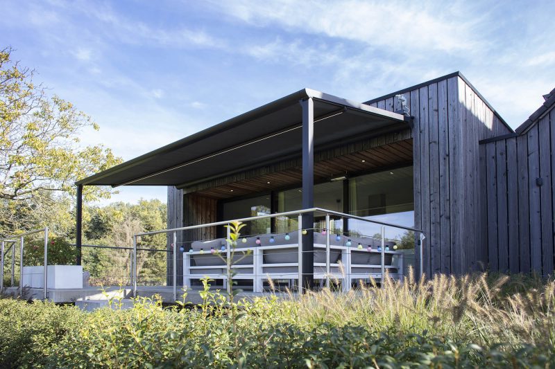 Bildet av et hus med pergolamarkise på utsiden. Det er på en terrasse med møbler.